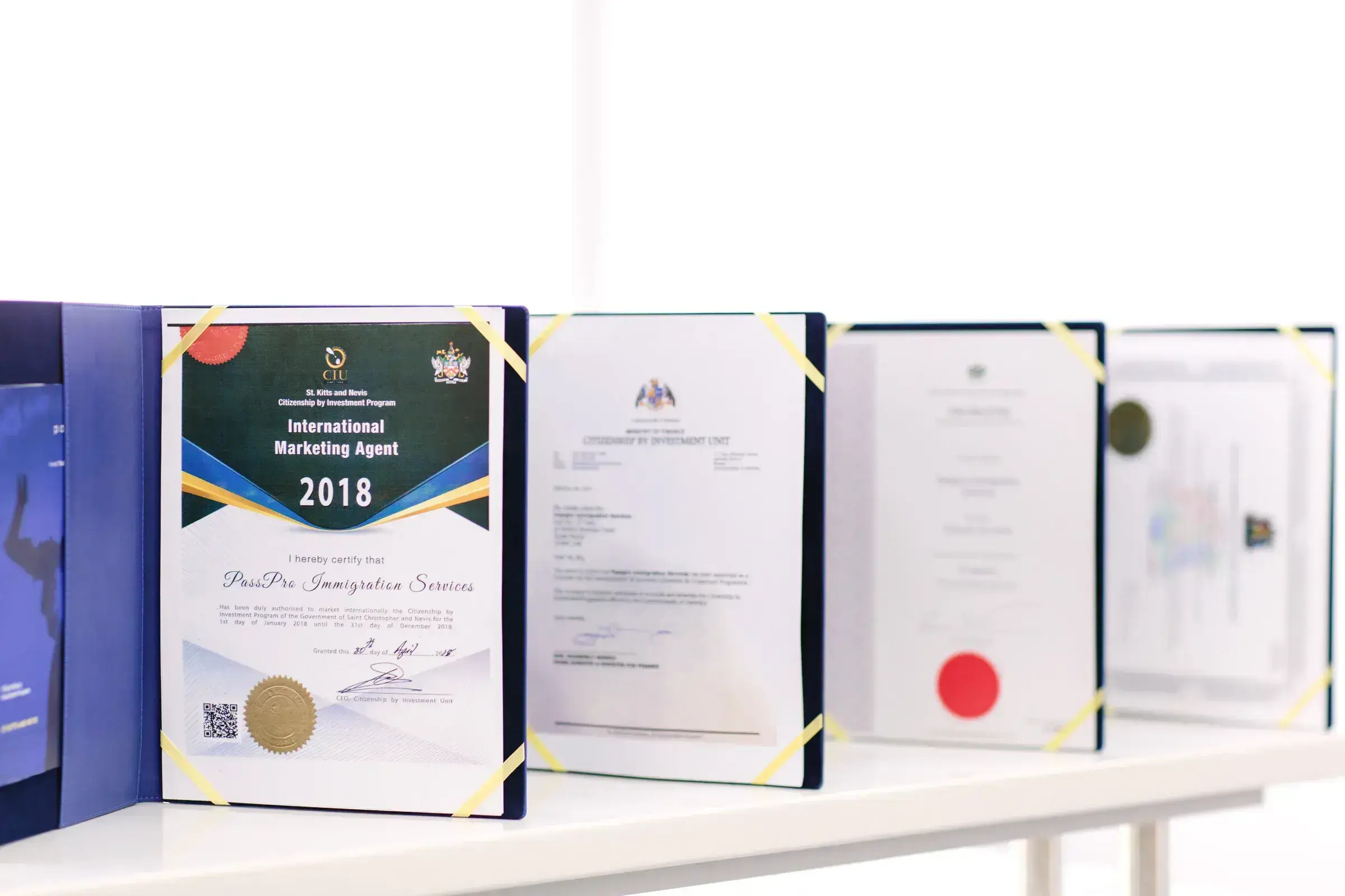 A row of PassPro's authorised-agent certificates from the five Caribbean Citizenship by Investment programmes, presented in navy folders.