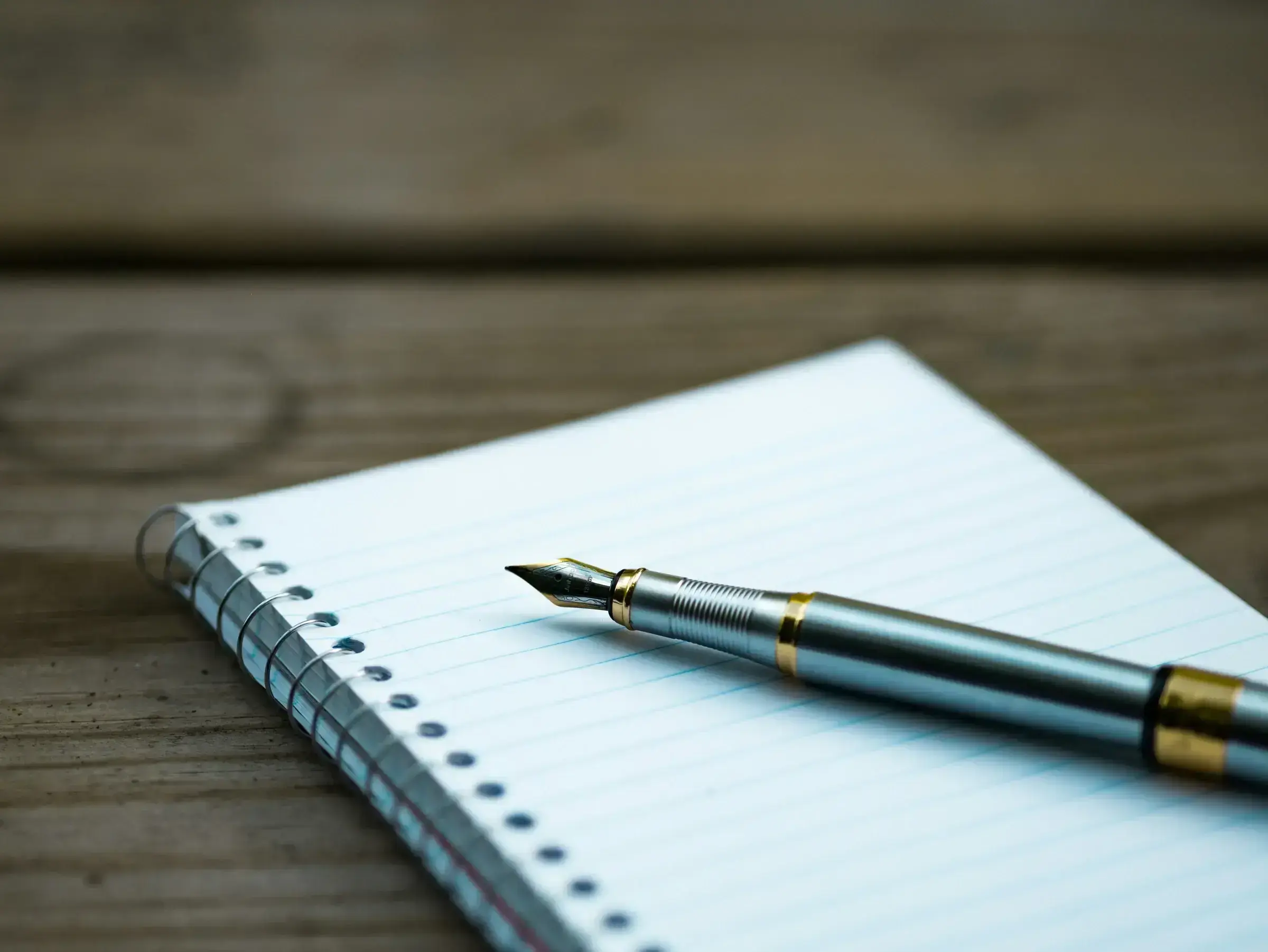 An open notebook and fountain pen resting on a desk in soft natural light — a quiet image of contemplation and deliberation.