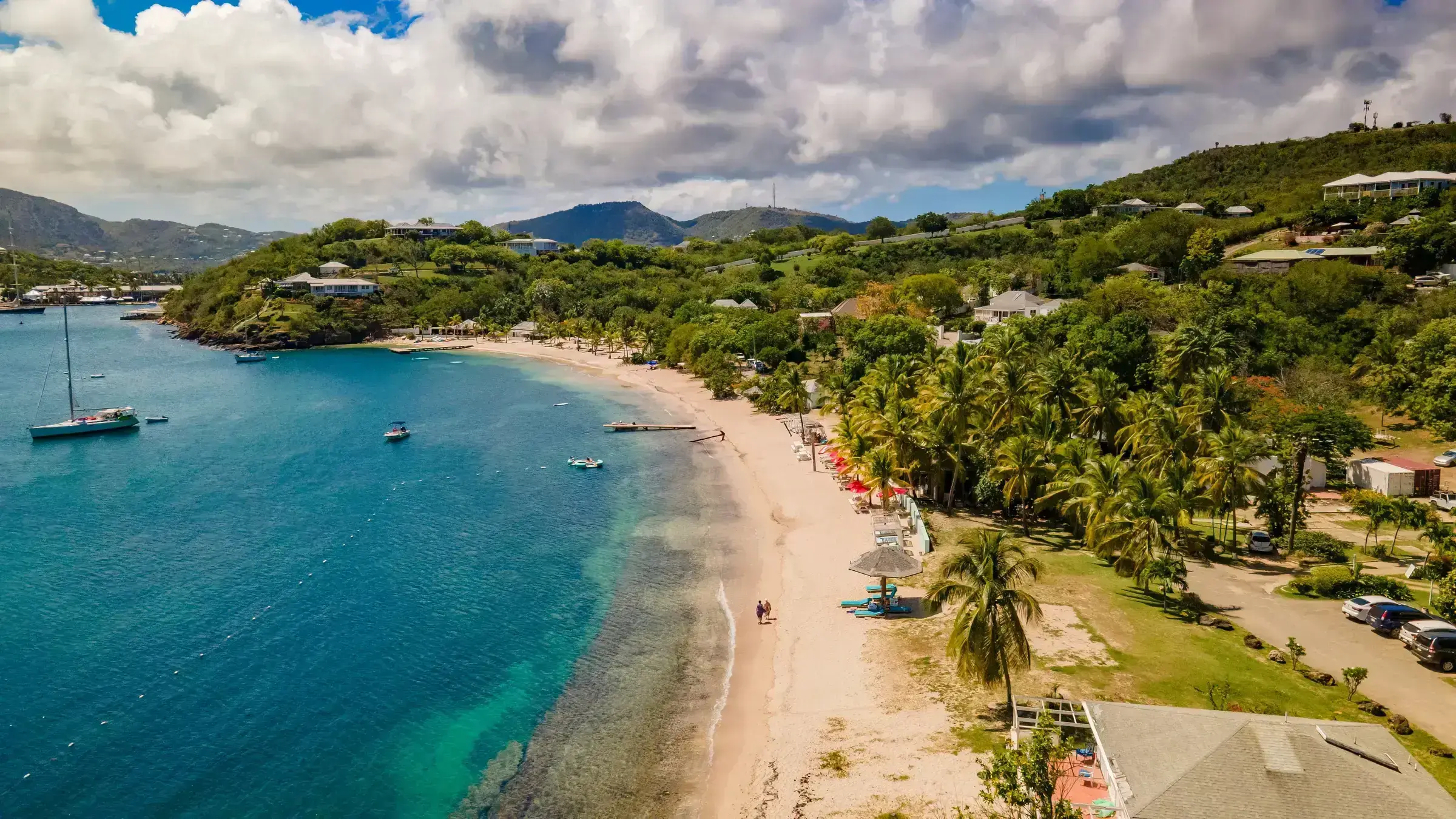 An Antigua harbour scene with sailing yachts at anchor and the soft pink of an Antiguan beach in the background.