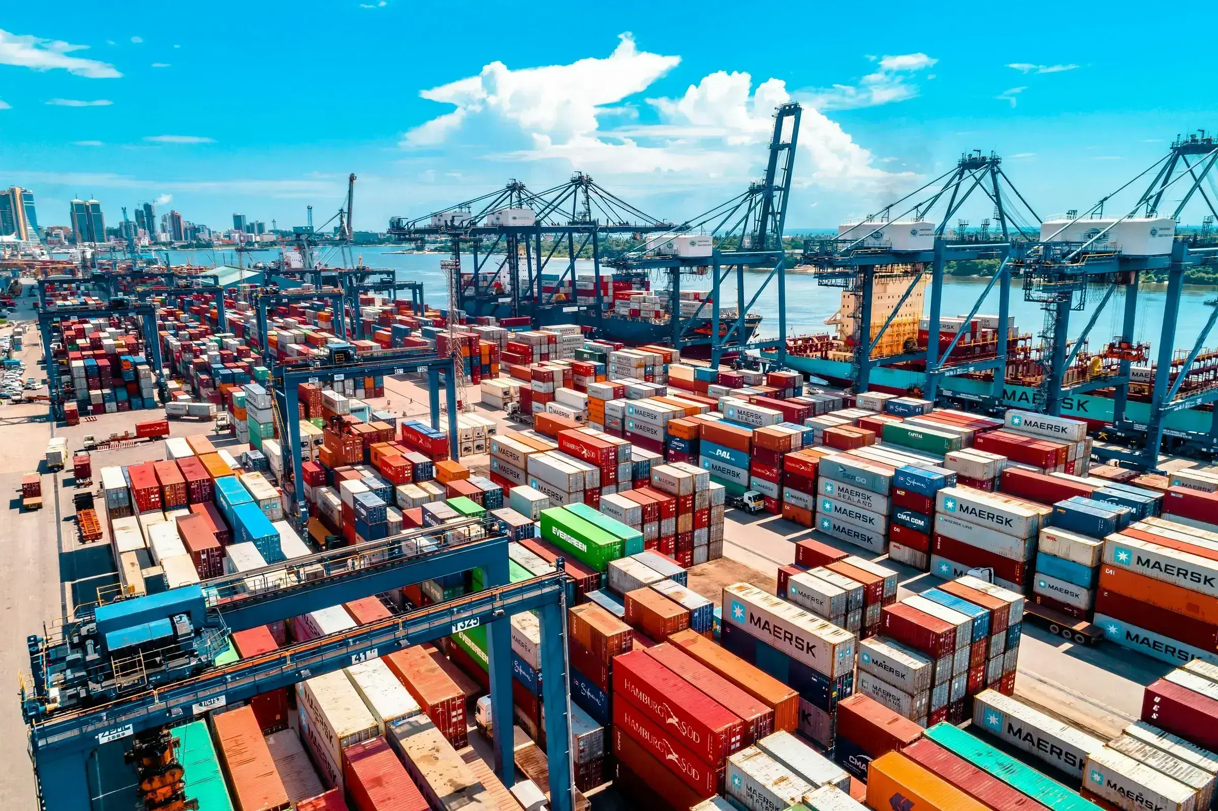 A tall stack of multicoloured shipping containers in a working port, photographed from below against an open sky.