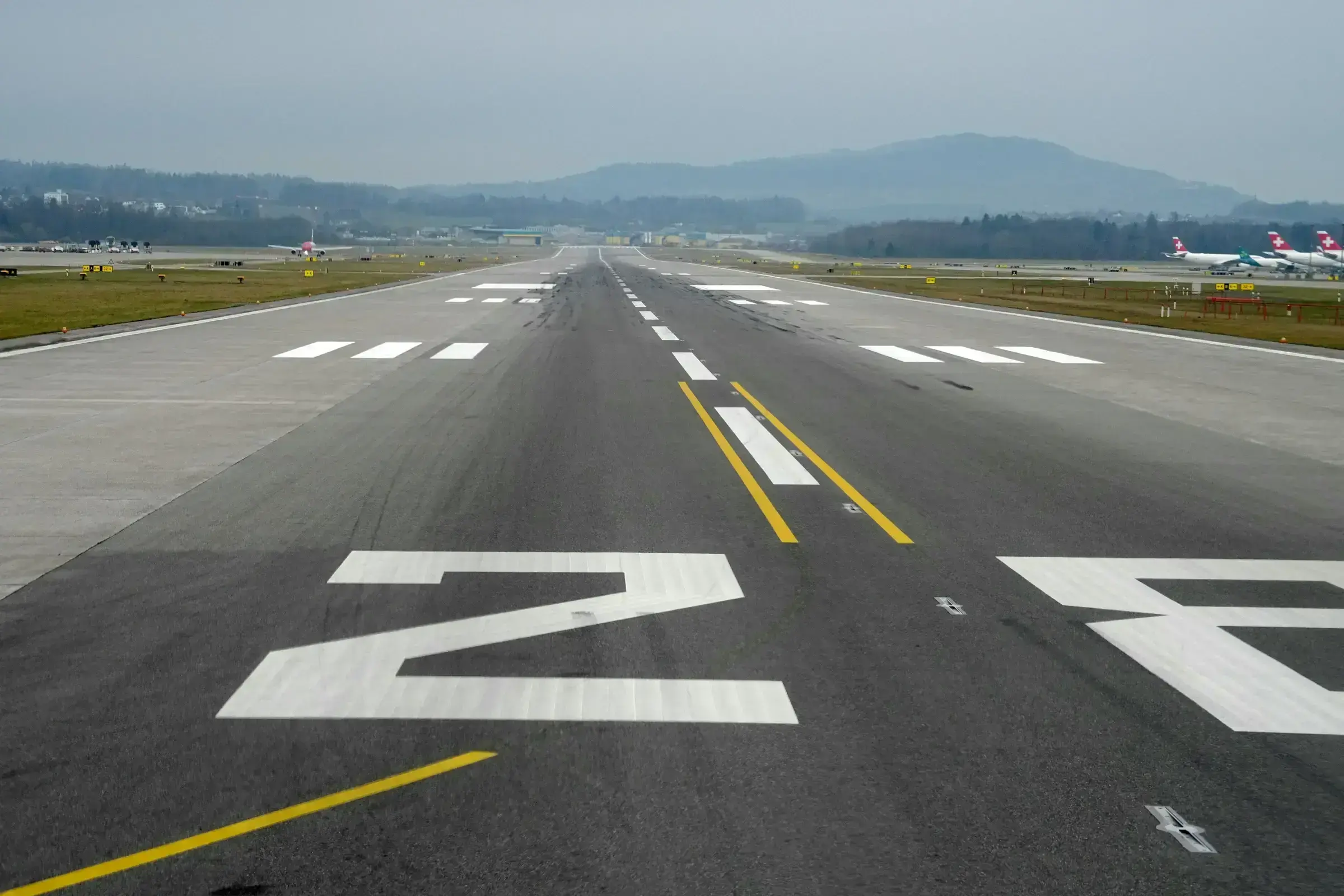 An airport runway at dusk with an aircraft approaching — the visual code of international networks and the talent that moves through them.
