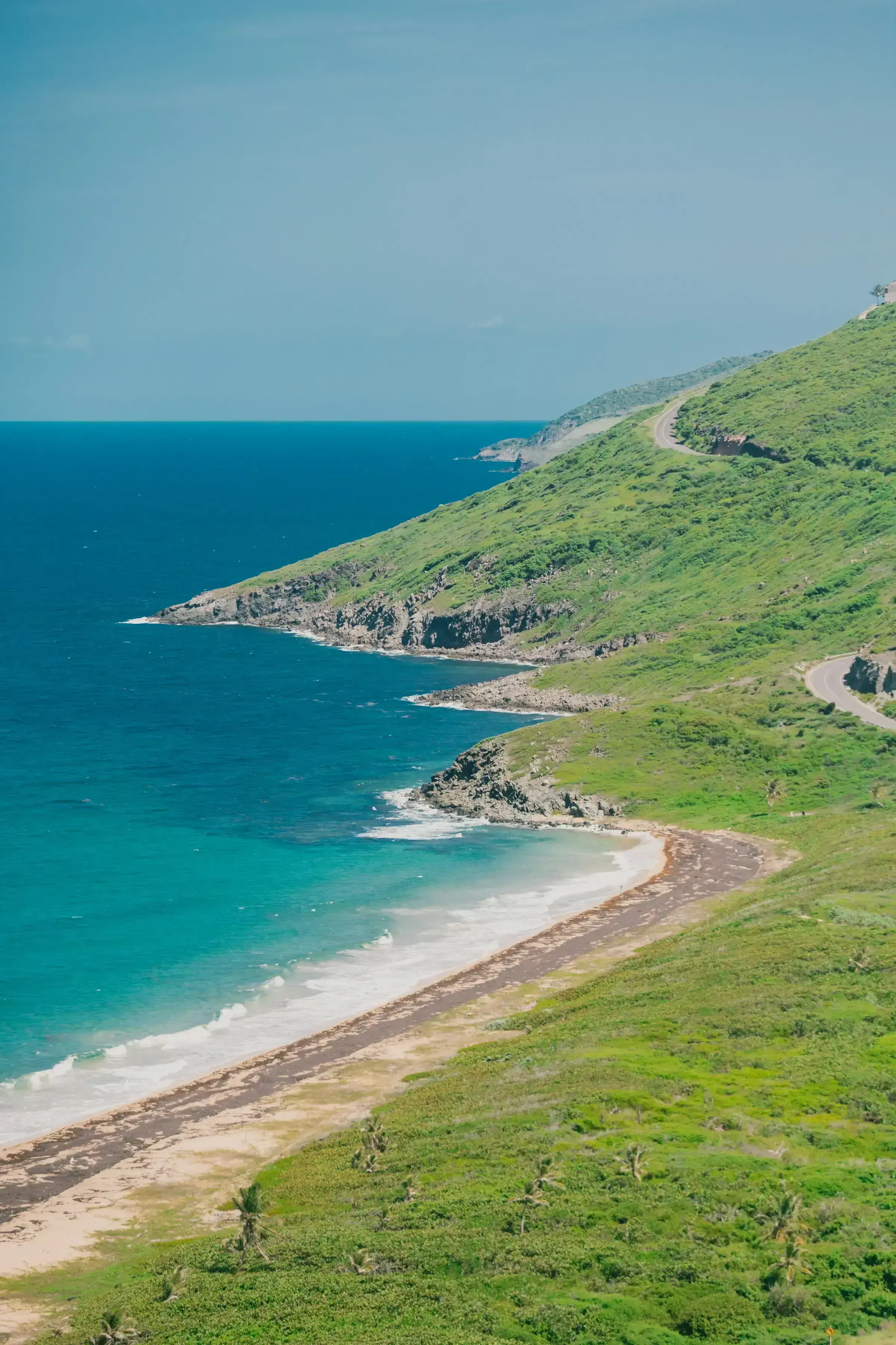 A winding road traversing a lush green coastal hillside in the Eastern Caribbean.