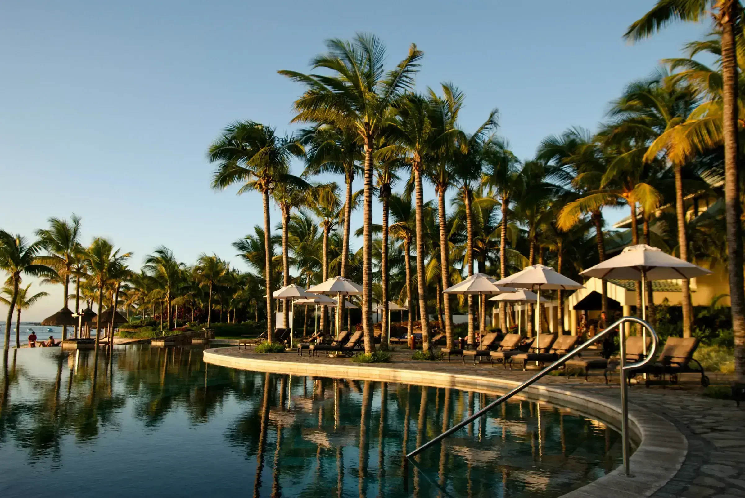 A luxury infinity pool at sunrise, framed by coconut palms — visual shorthand for the upmarket end of the Caribbean real-estate landscape.