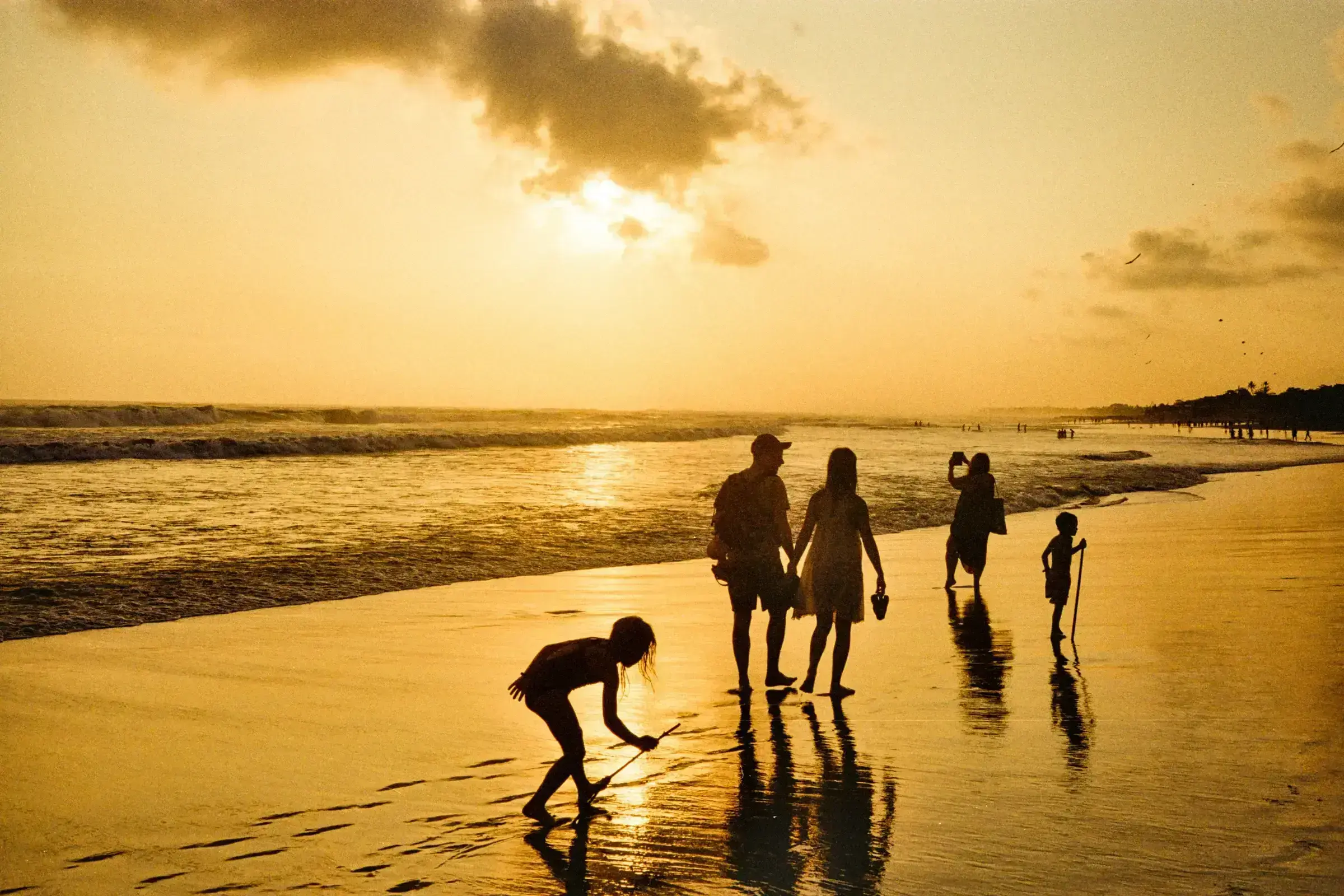 A Caribbean family-coded scene — a wide beach at golden hour, framed by palms.