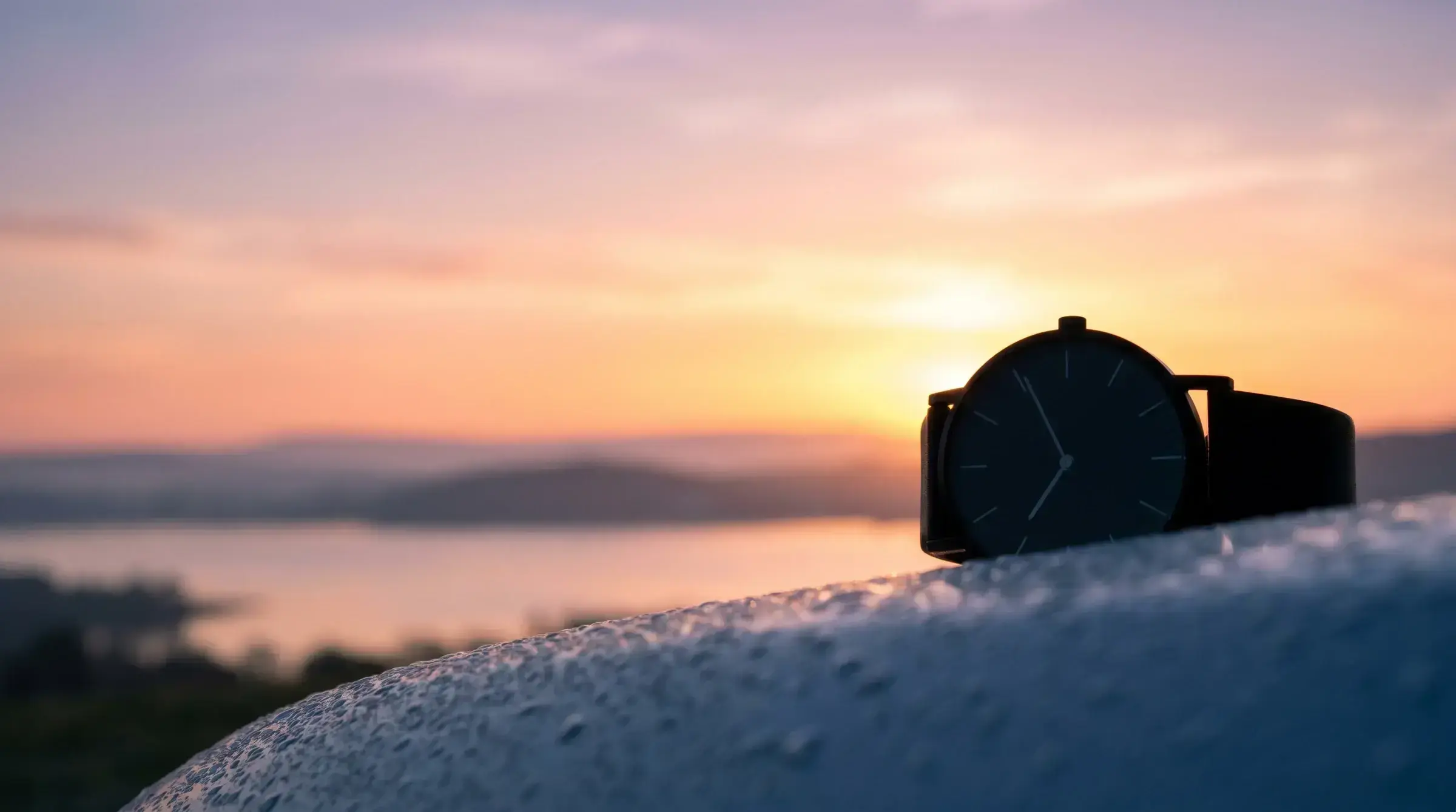 A modernist wristwatch silhouette against a golden sunrise — the visual code of accelerated processing.