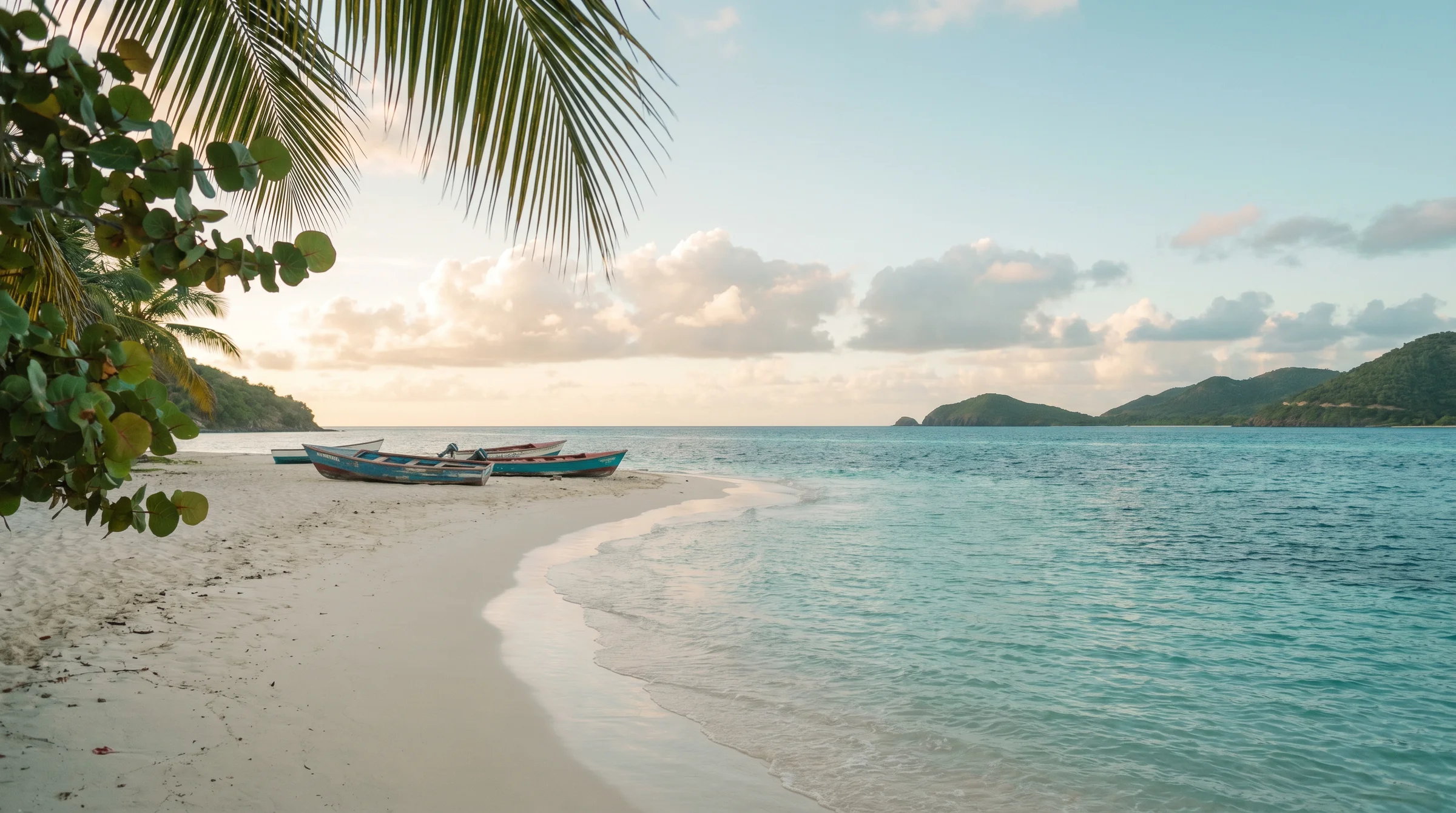 A Caribbean beach in soft afternoon light — sand, turquoise water, palm shadow.